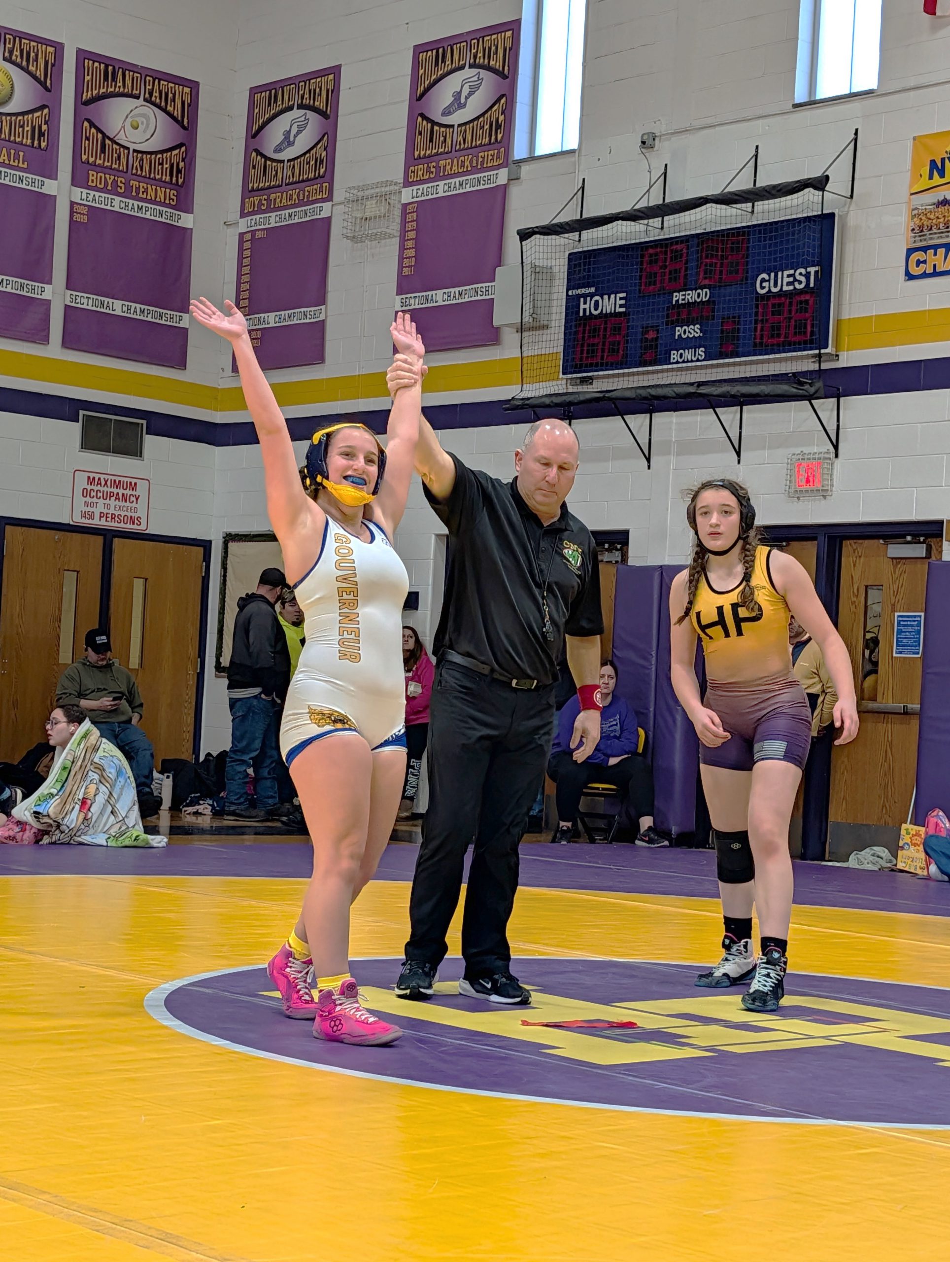 Two female high school wrestlers with adult male holding the winners hand up