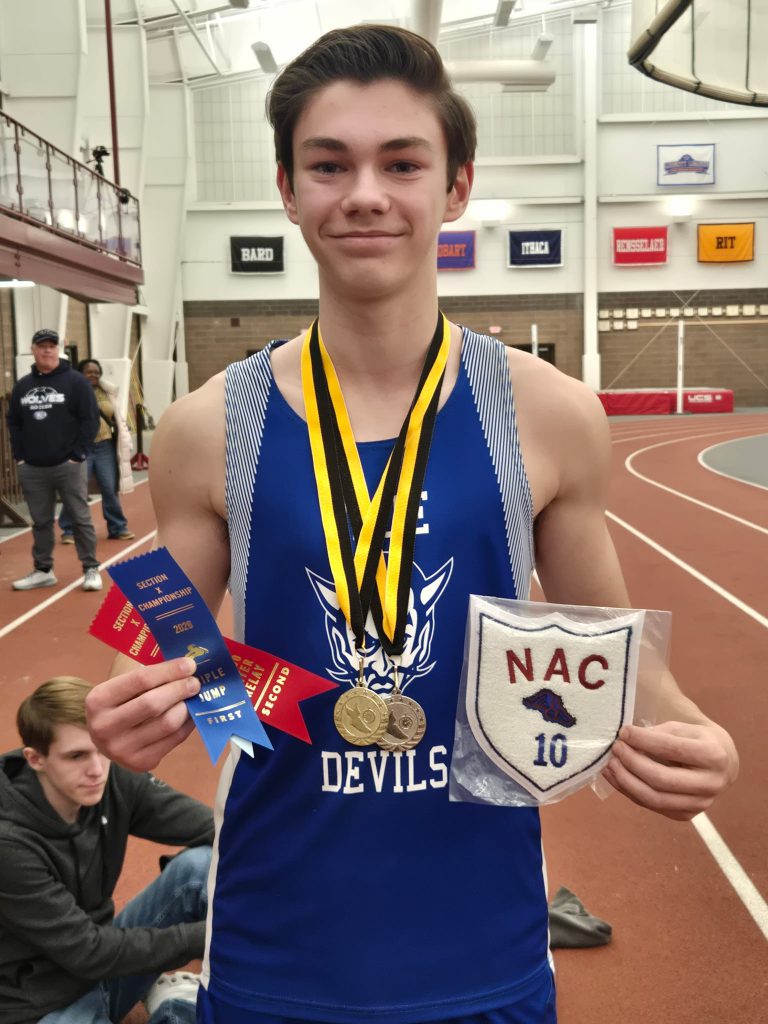 Male indoor track and field athlete holding a patch and ribbons