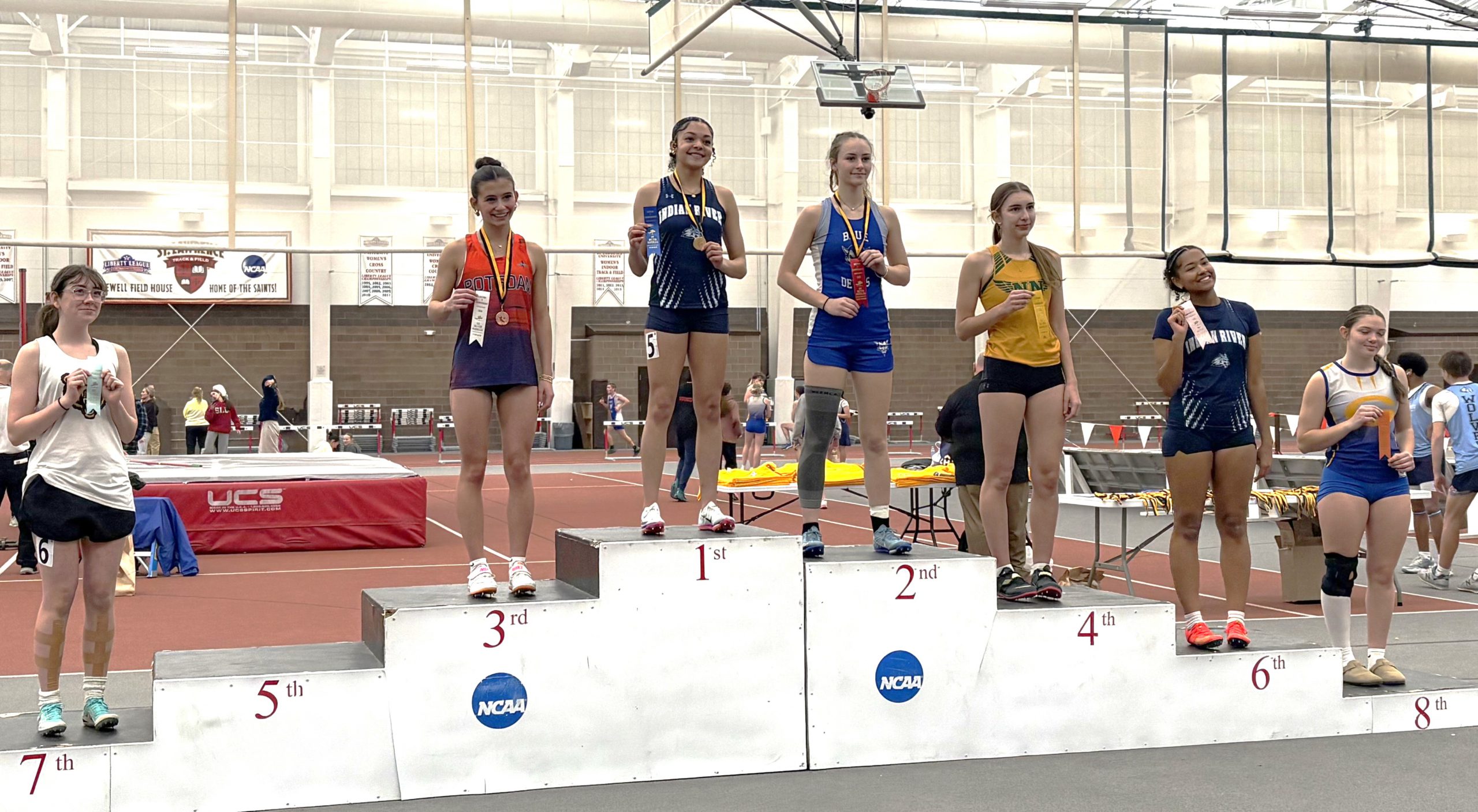High school female indoor track and field athletes standing on finisher's podium holding ribbons