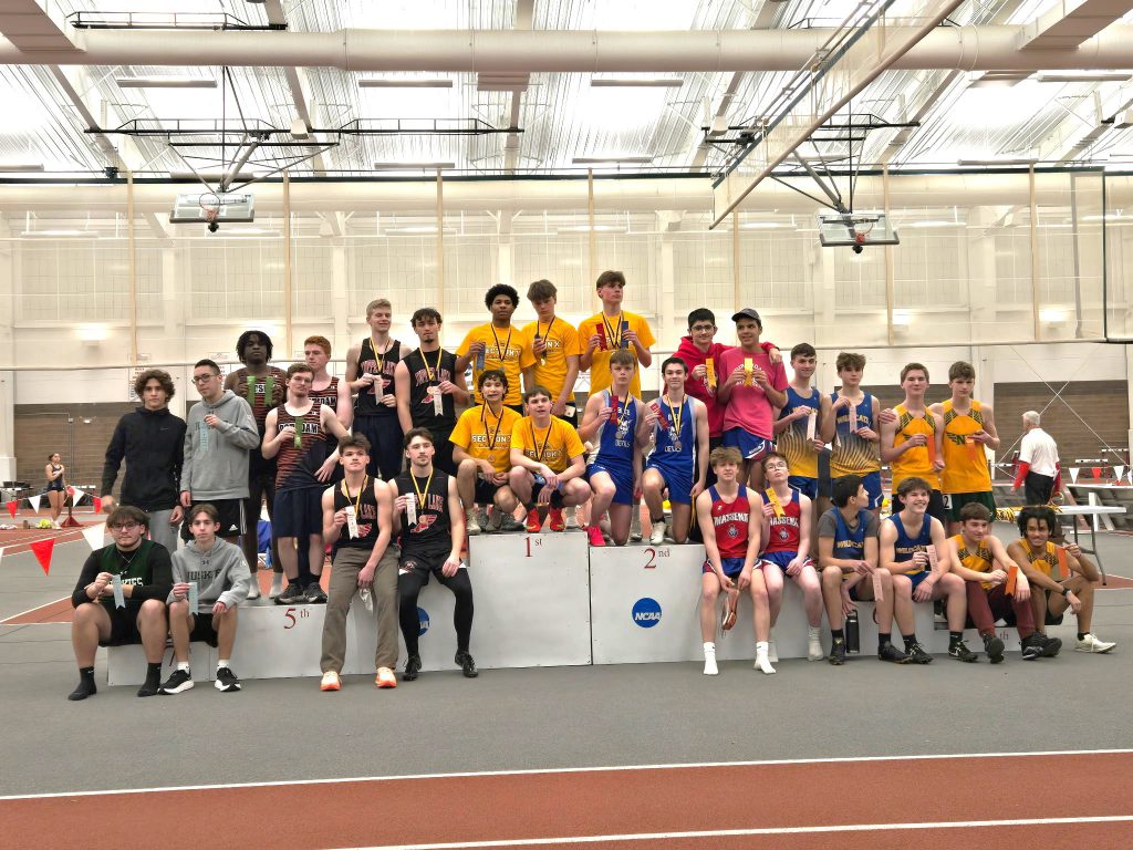 Large group of male indoor track and field athletes on a podium holding ribbons