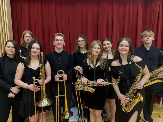 Small group of high school students smiling wearing black and holding musical instruments