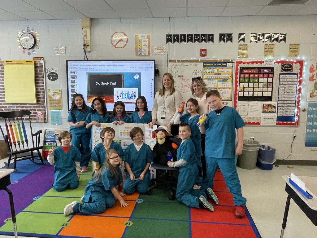 Small group of elementary students wearing blue hospital scrubs with two adult females