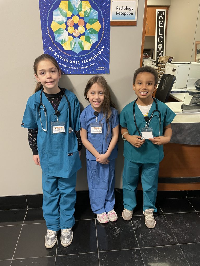 Elementary students wearing blue and green hospital scrubs smiling