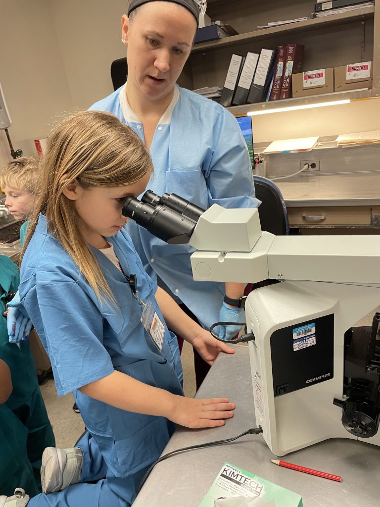Female elementary student wearing blue hospital scrubs looking through hospital equipment with an adult female