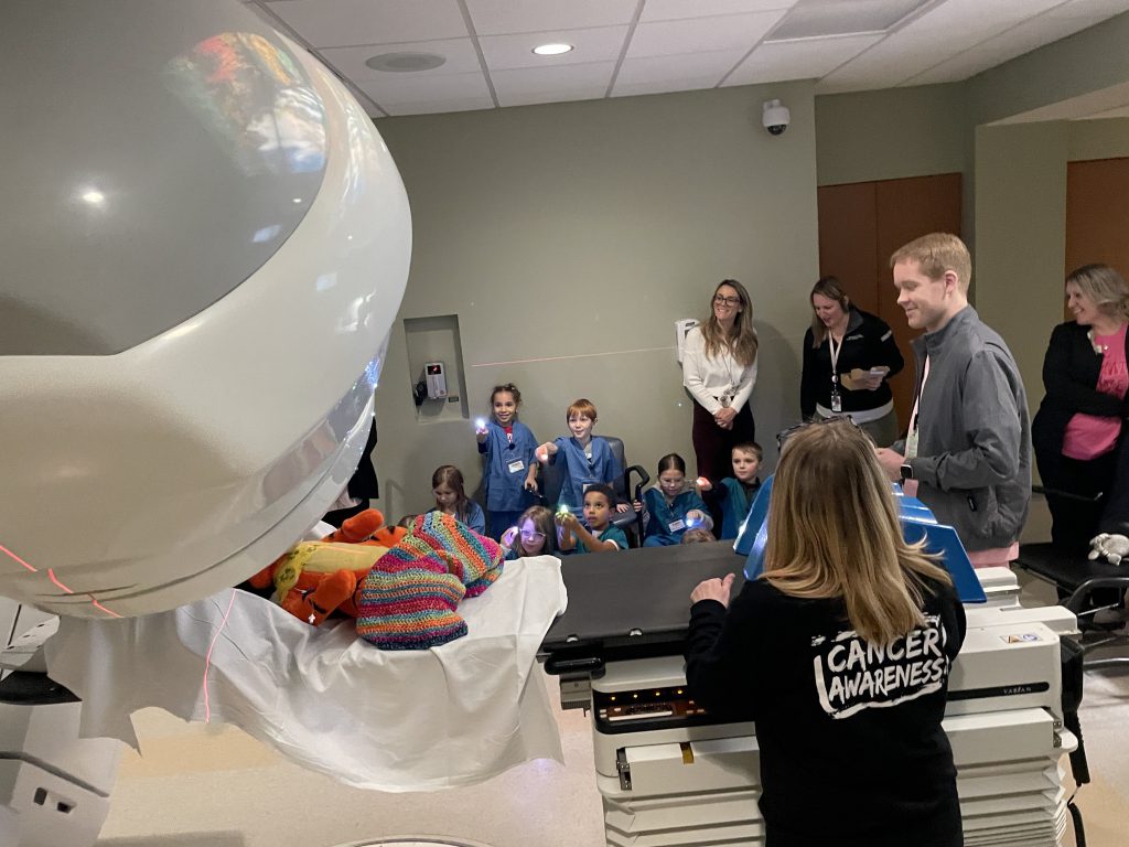Small group of elementary students wearing blue and green hospital scrubs looking at medical equipment with adults