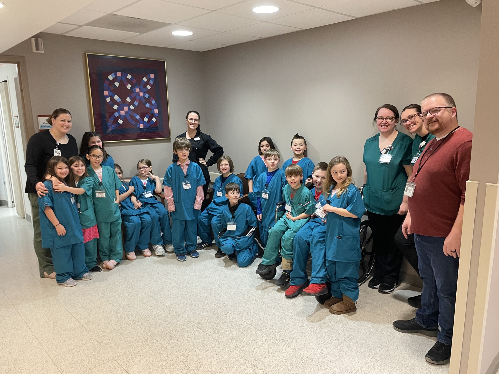 Small group of elementary students wearing green and blue hospital scrubs with teachers and adults