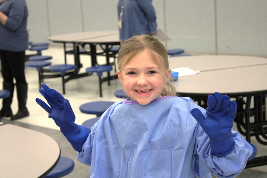 Female elementary student smiling with blue hospital scrubs and gloves