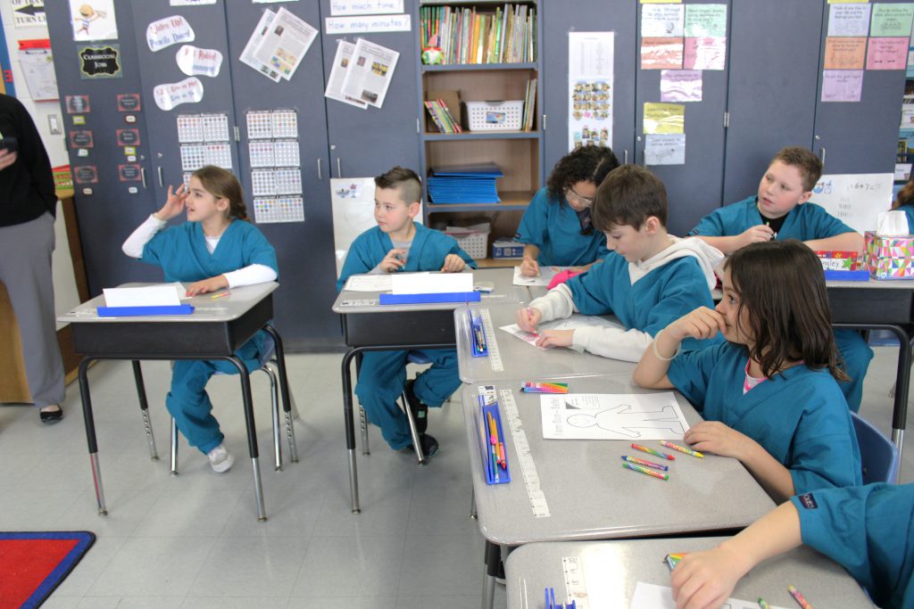 Small group of elementary students wearing blue hospital scrubs coloring
