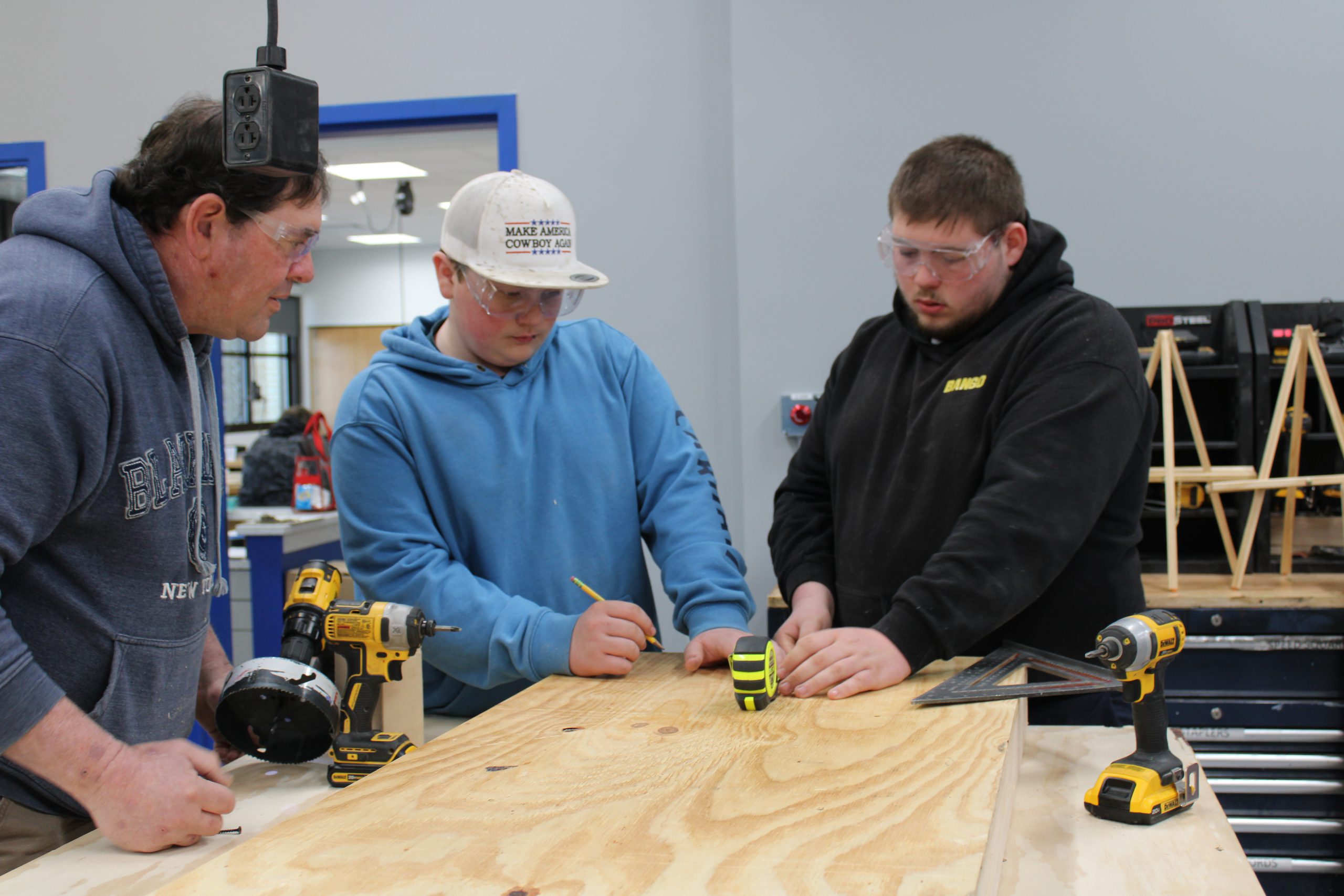 Two male high school students working on a project with an adult male teacher assisting