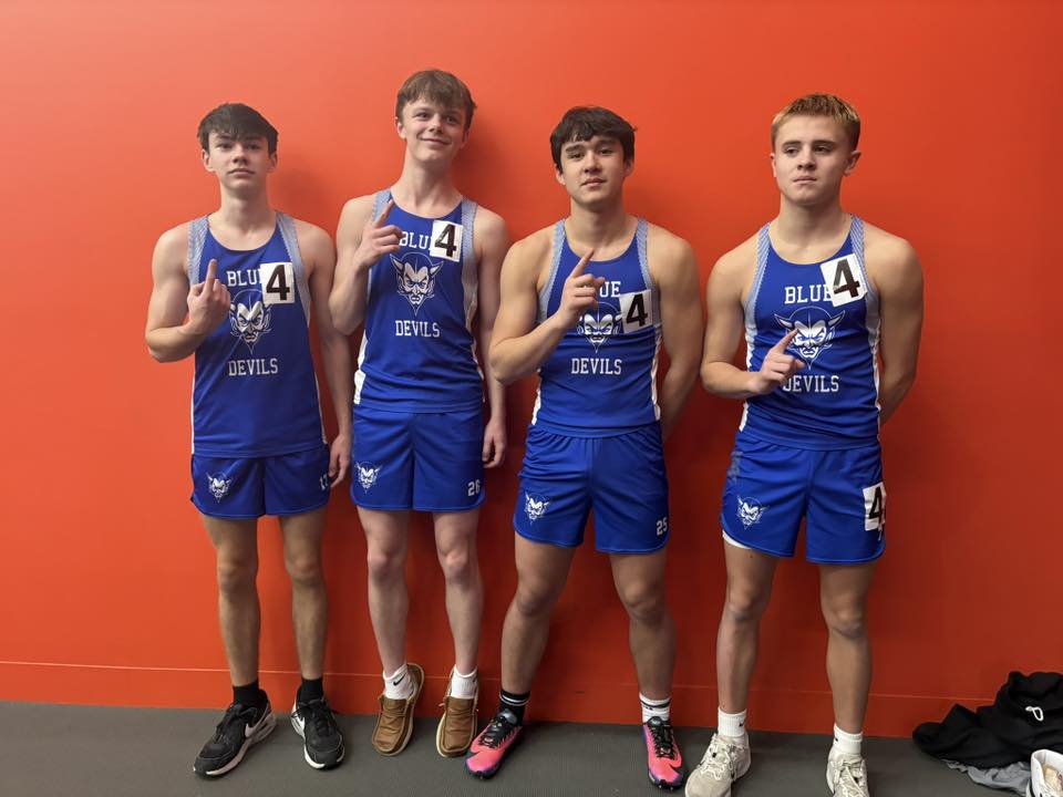 Four male high school indoor track and field athletes wearing blue singlets showing one finger