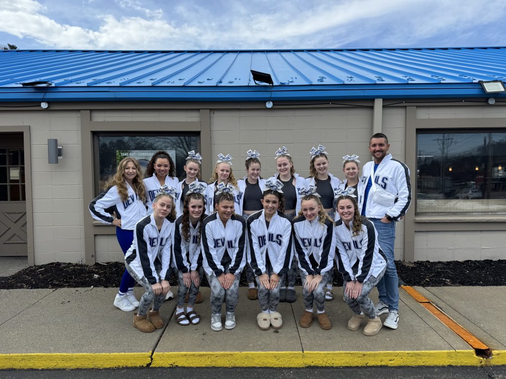Small group of female high school cheerleaders and a male and female coach wearing white jackets
