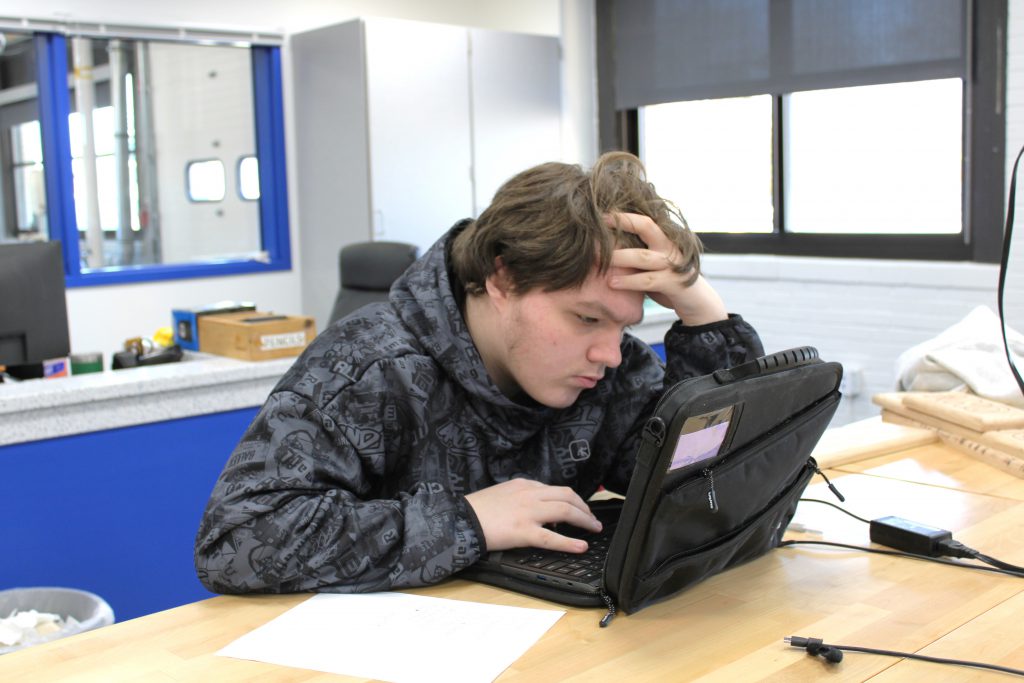 Male high school student working on a laptop sitting at a wooden desk