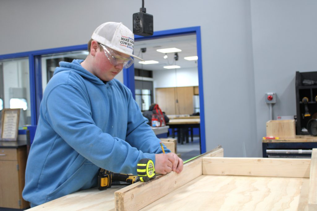 Male high school student using a measuring tap and pencil