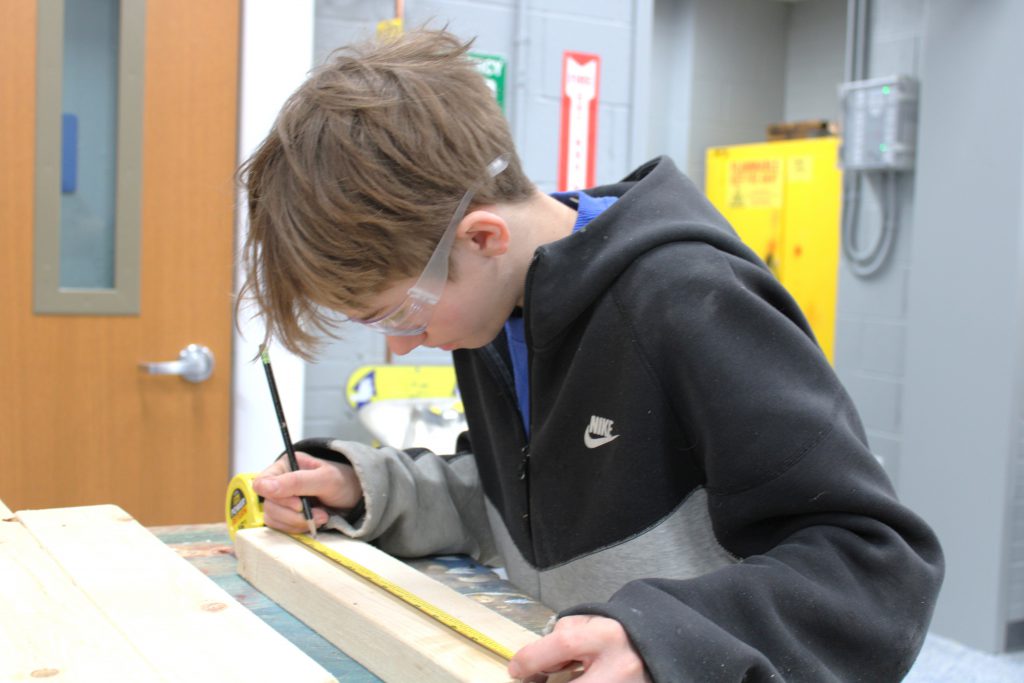 Male high school student using a pencil and measuring tape