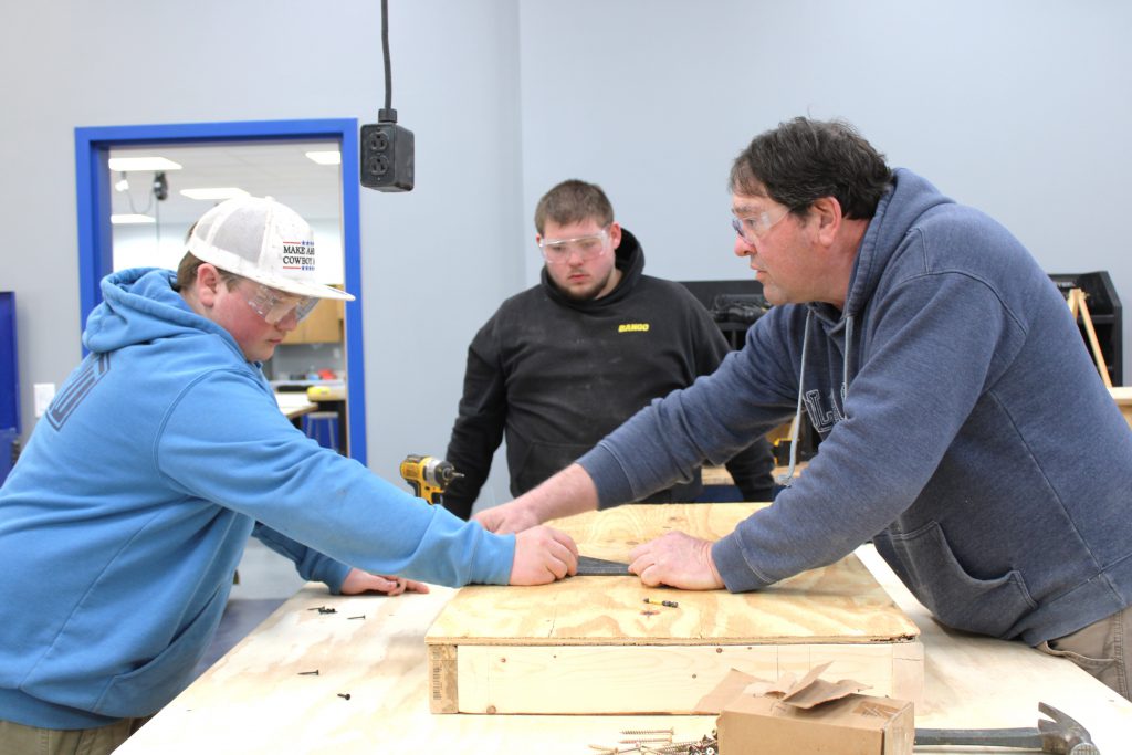 Two male high school students working on a project with assistance from male teacher