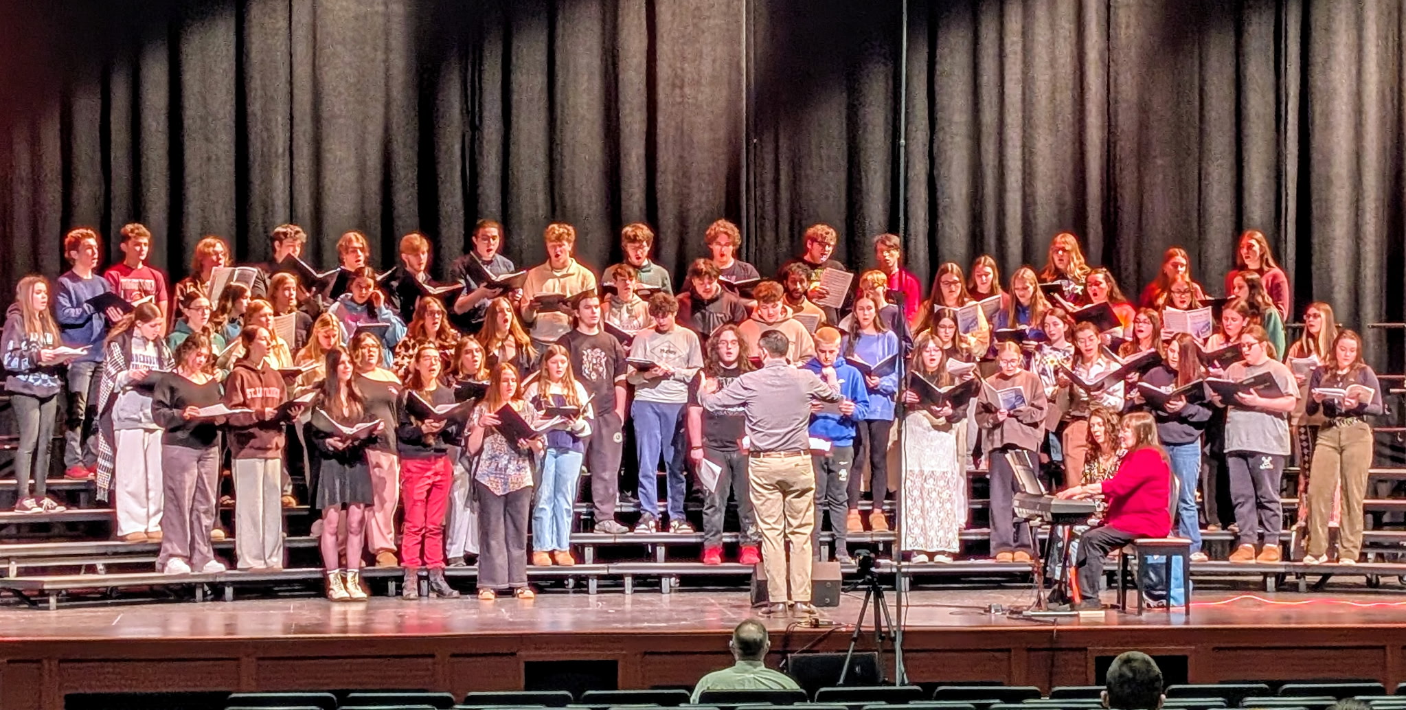 Large group of students holding music books and performing on stage