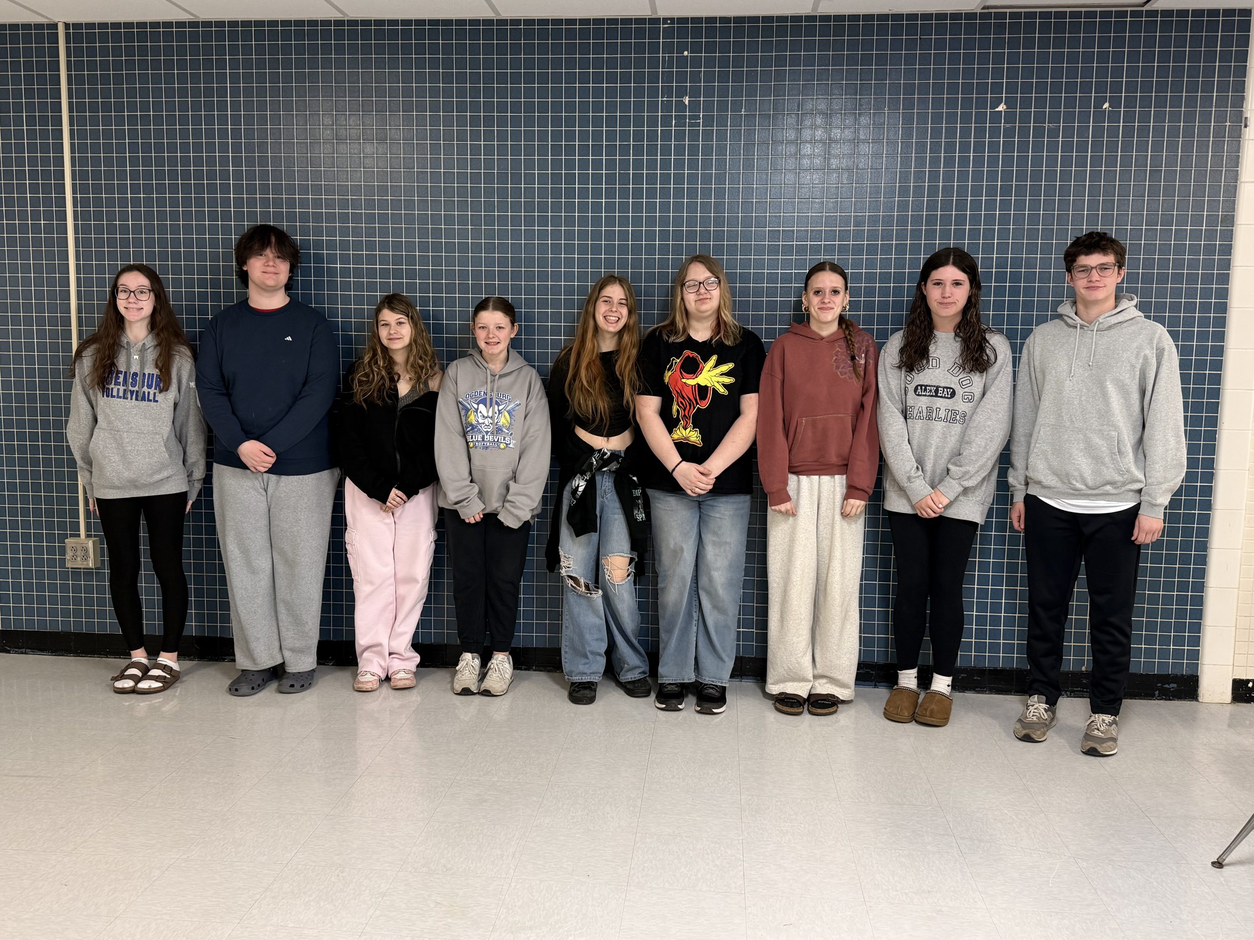 Small group of high school students standing against a blue wall smiling