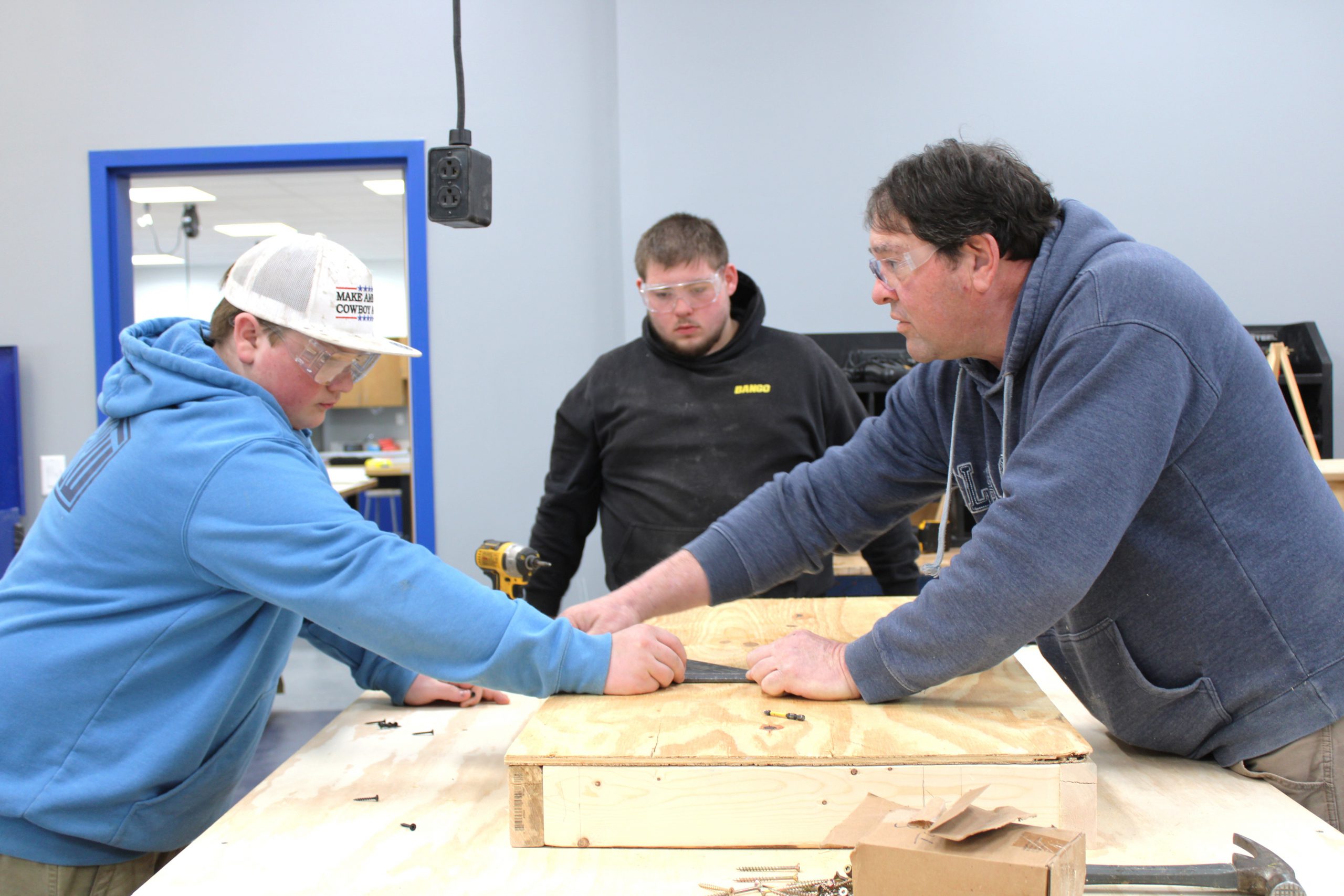 Two male students working on a project with an adult male teacher