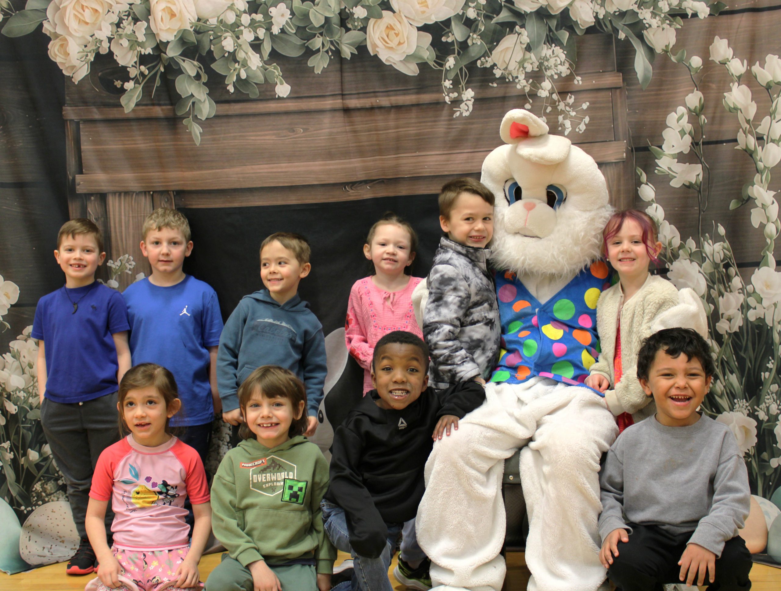 Small group of young students sitting and standing while smiling and next to a person in a bunny outfit
