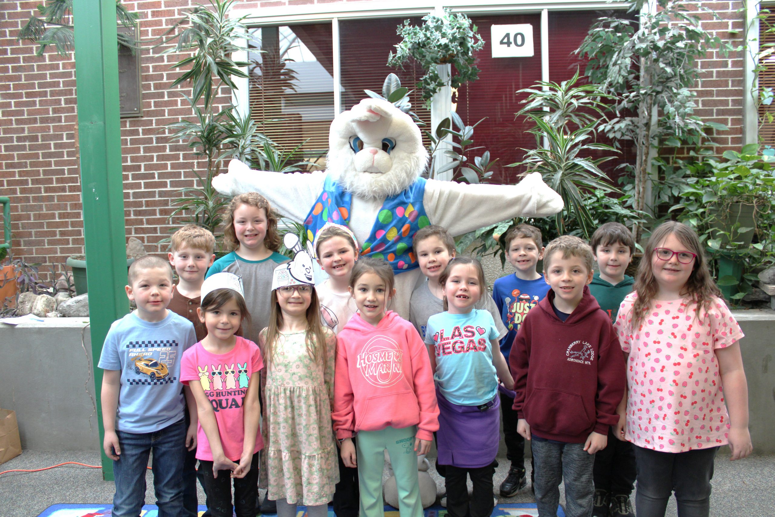 Young students standing and smiling next to a person wearing a bunny outfit