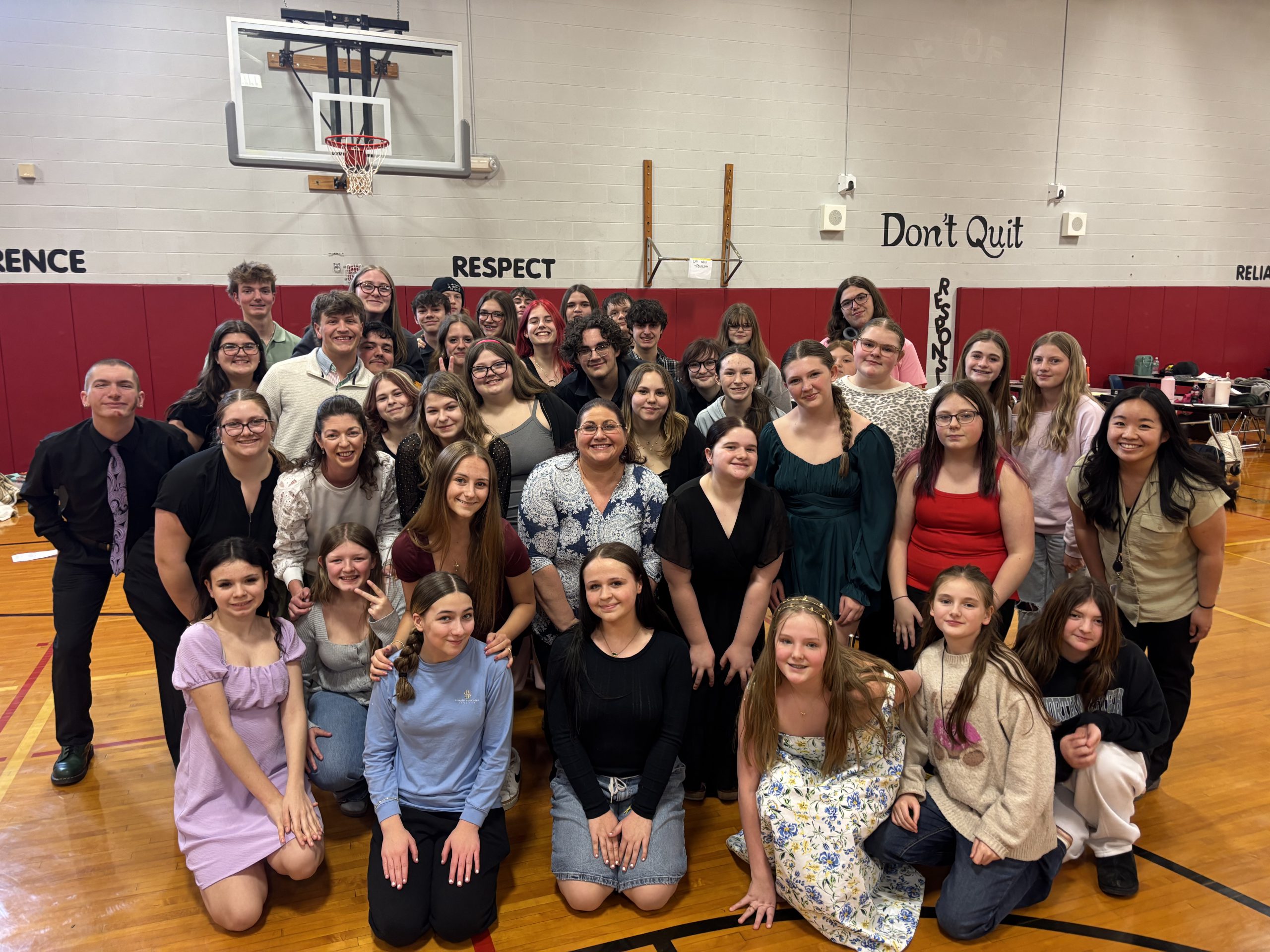 Large group of high school students standing and kneeling in a gymnasium smiling