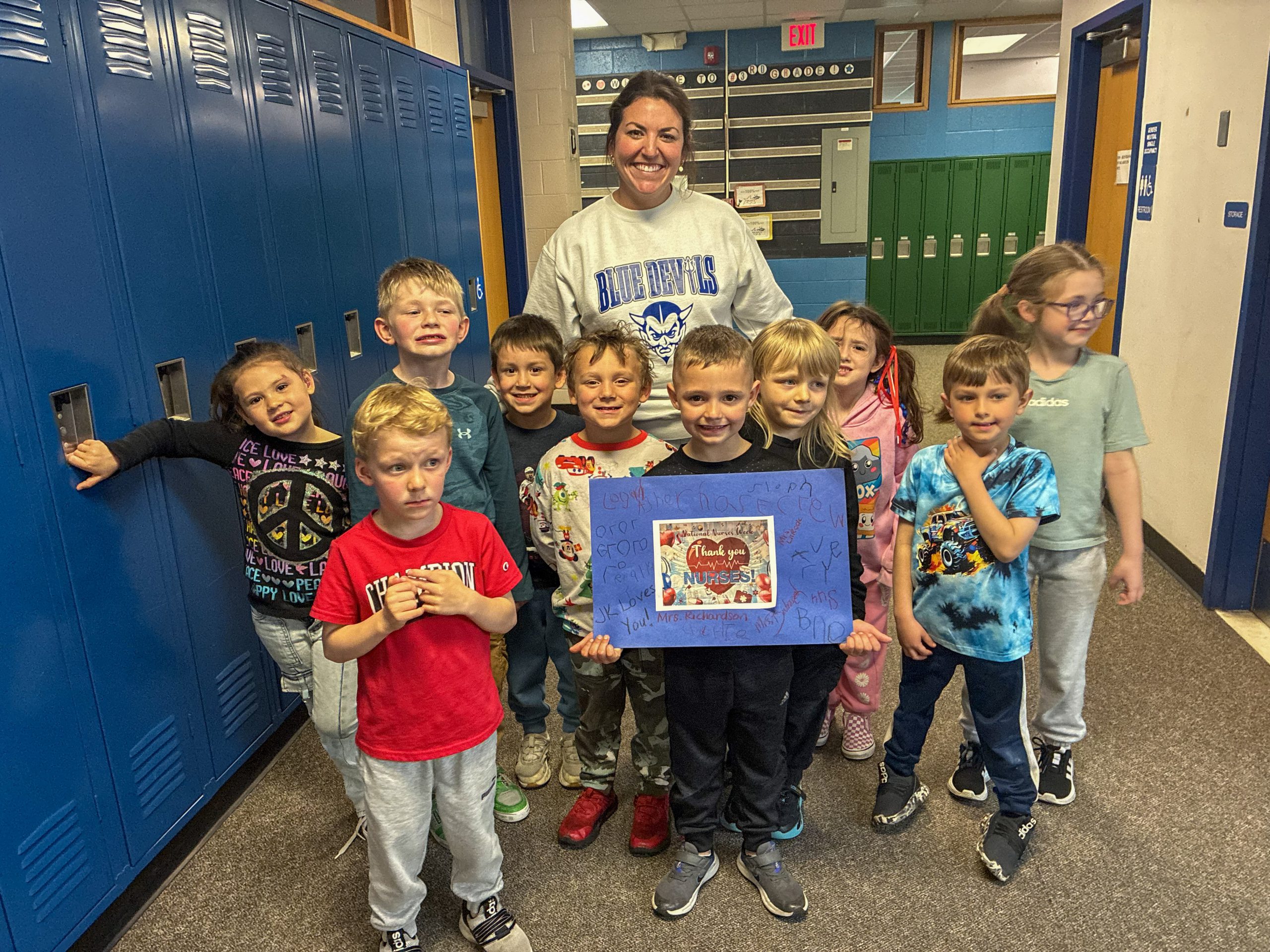 Small group of young students with adult female smiling with one student holding a blue piece of paper with a decorative card